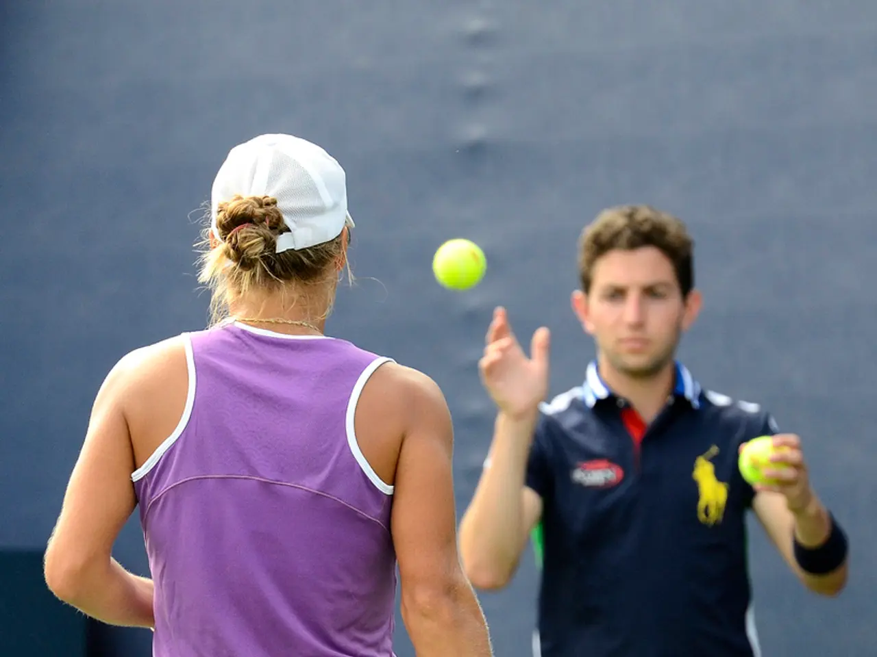 In this image there are two players. In the left side a woman holding a racket is standing. She is...