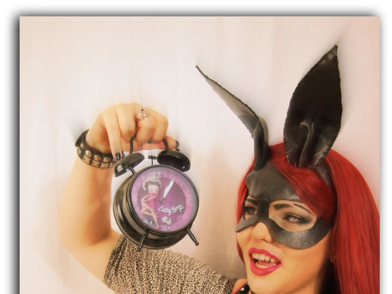 In this image I can see a woman wearing a mask and holding an alarm clock.