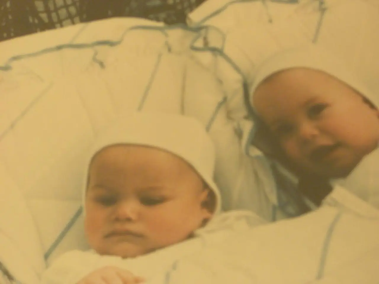 In this image we can see two babes are laying on pillows.