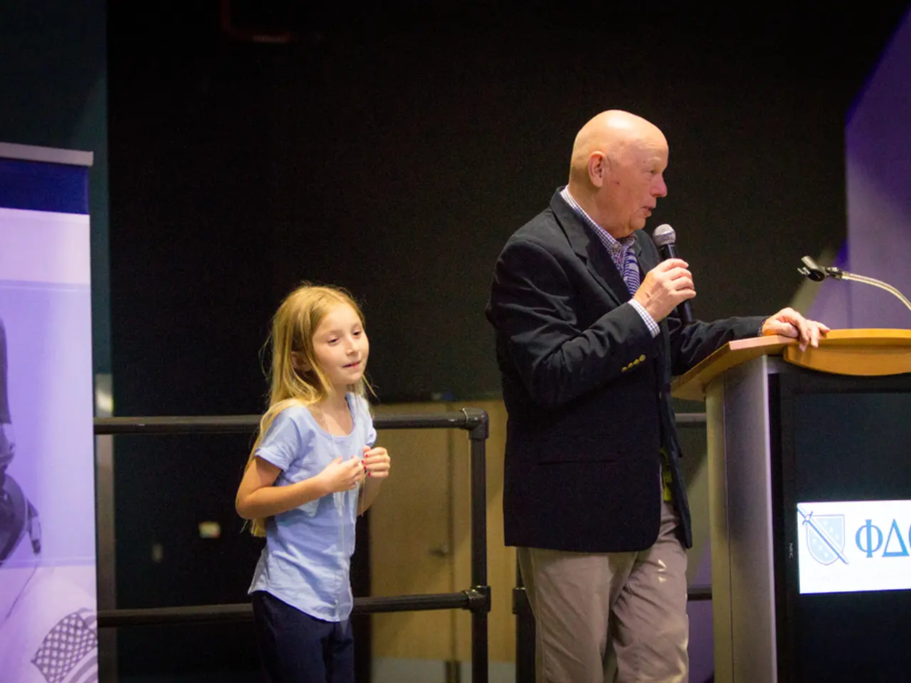 In this picture there is a man standing and holding a microphone, in front of him we can see stand...