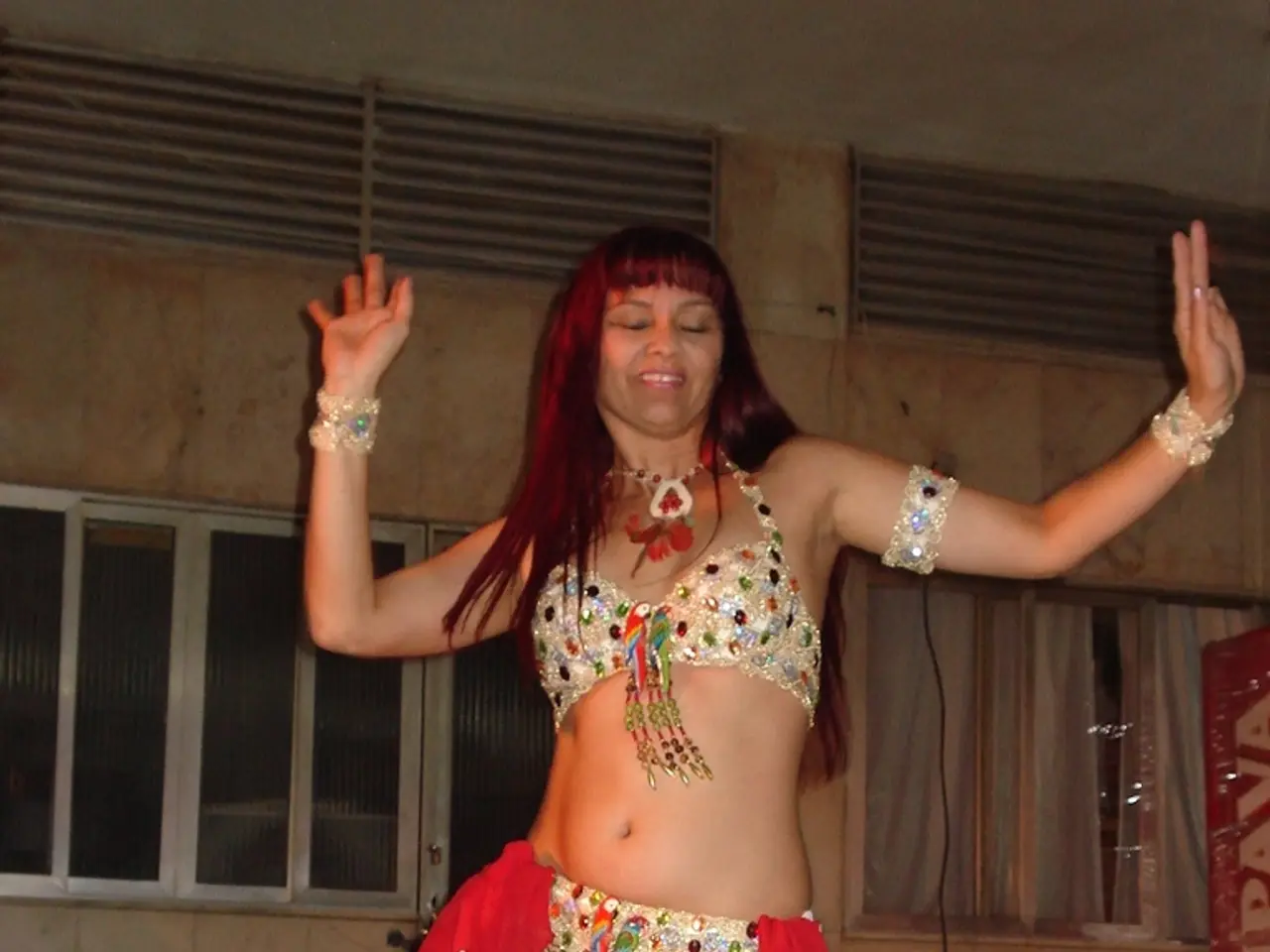 In the image there is a woman in gown doing belly dance and behind her there are windows on the...