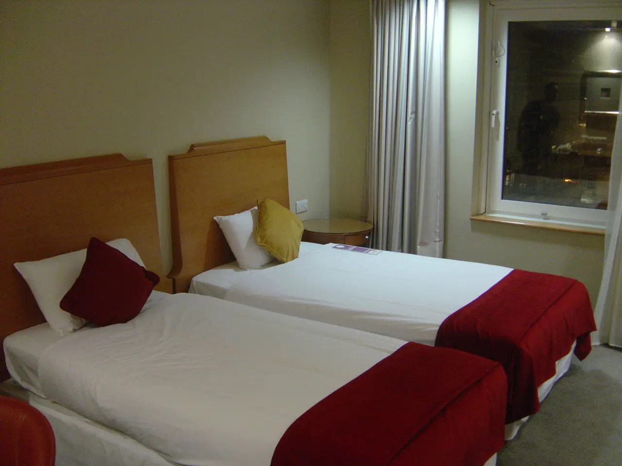 This is a picture of a bed room where there are 2 beds , 2 pillows , curtain and a window.