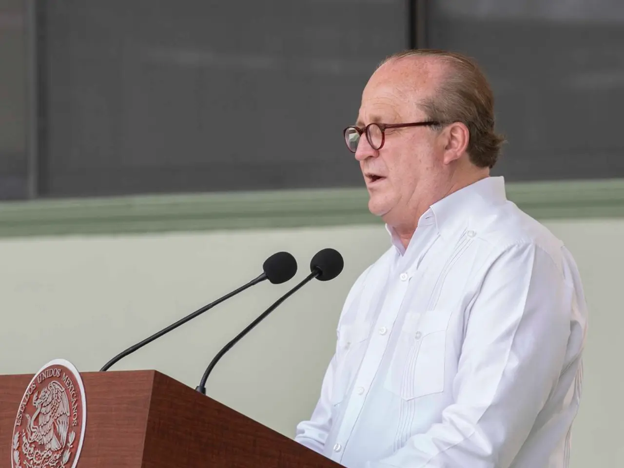 On the right side a man is standing near the podium and speaking, he wore a white color shirt,...