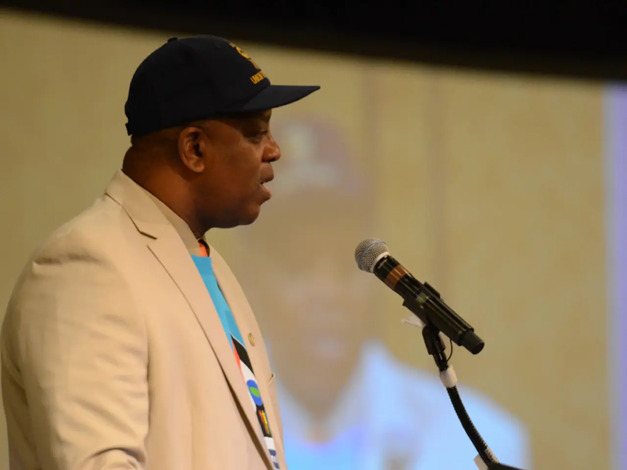 This picture is mainly highlighted with a man. He is wearing a black cap. He is standing and giving...