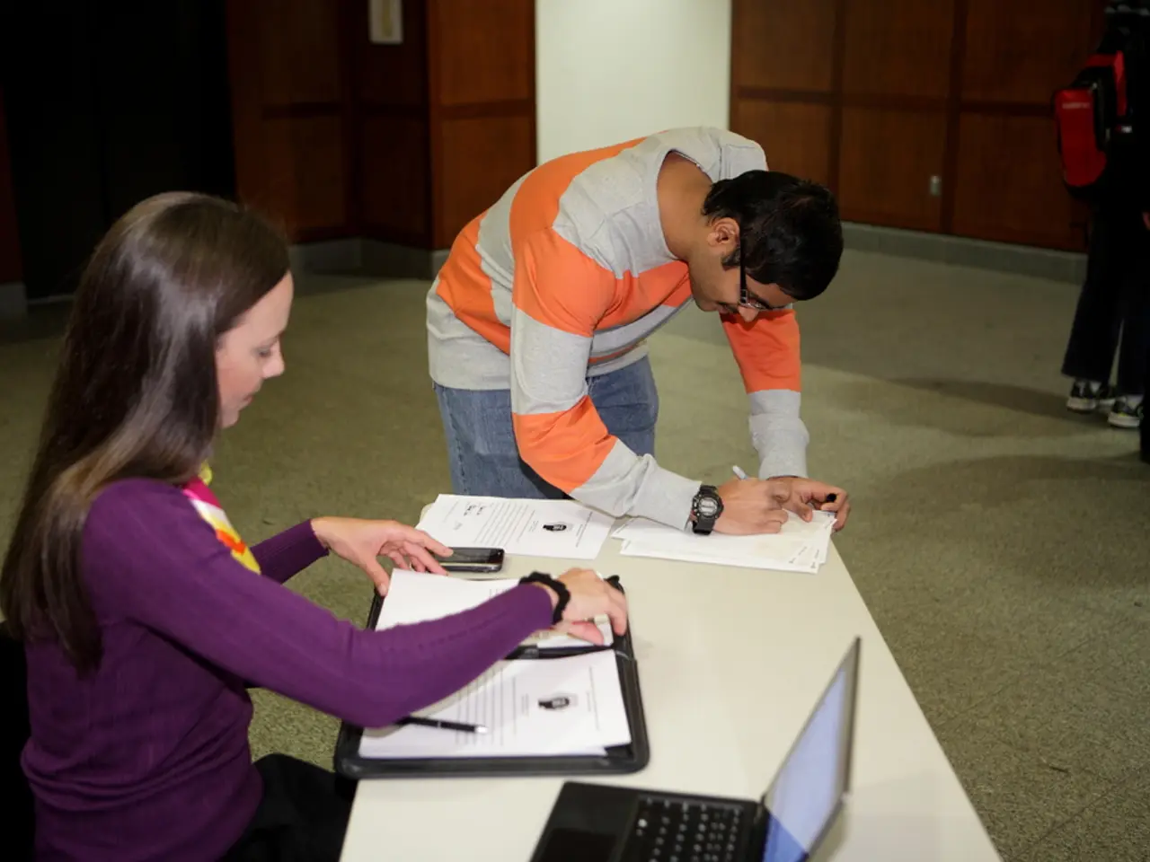 On the left side, there is a woman in a violet colored t-shirt, sitting on a chair, watching...