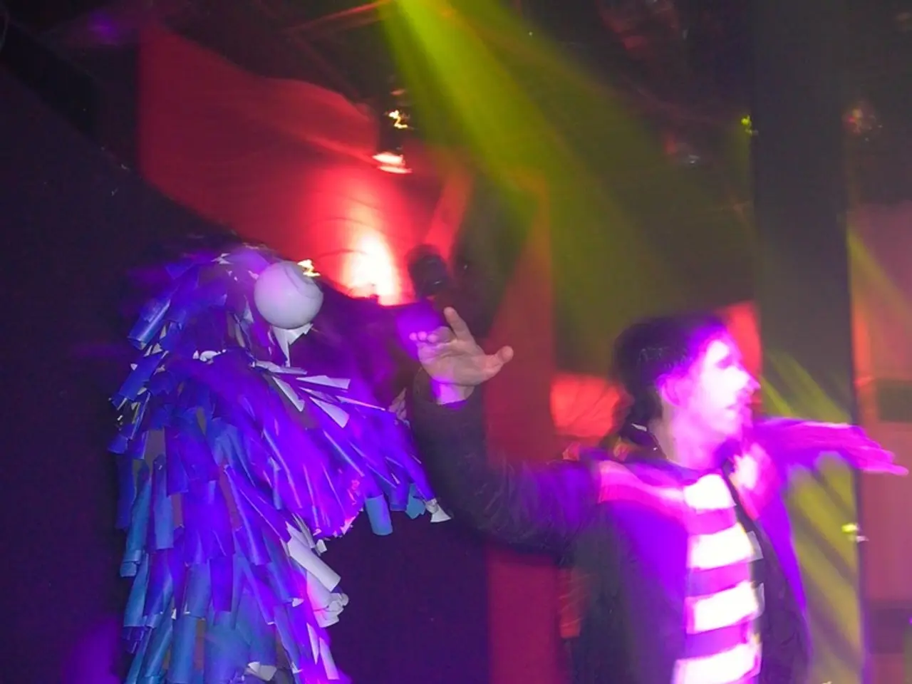 In this image, we can see some people dancing on the stage and a person who is on the left side...