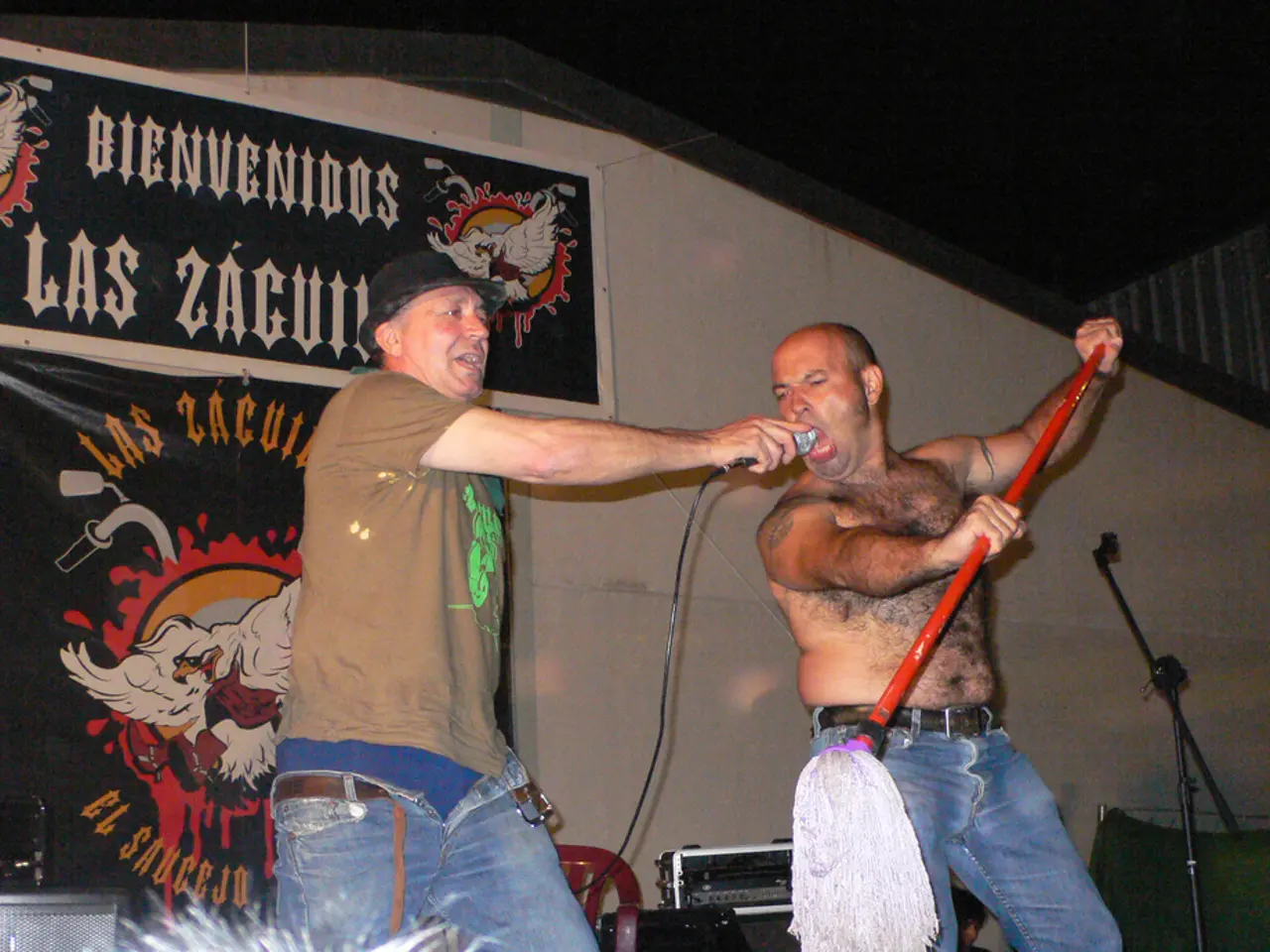 The picture is taken during a stage performance. In this picture there are two men standing on the...