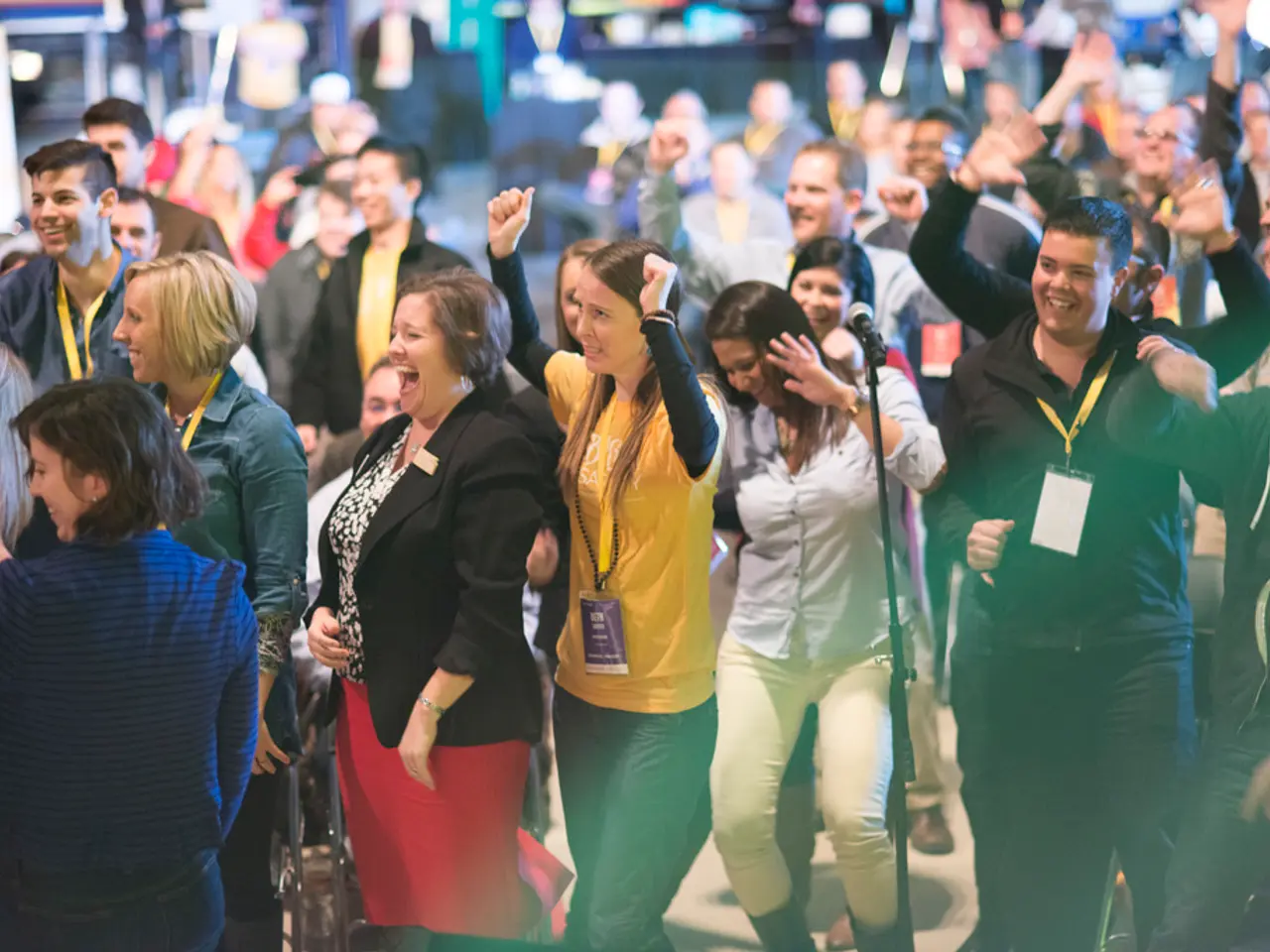 In the center of the image we can see many people standing and laughing. There is a mic placed on...