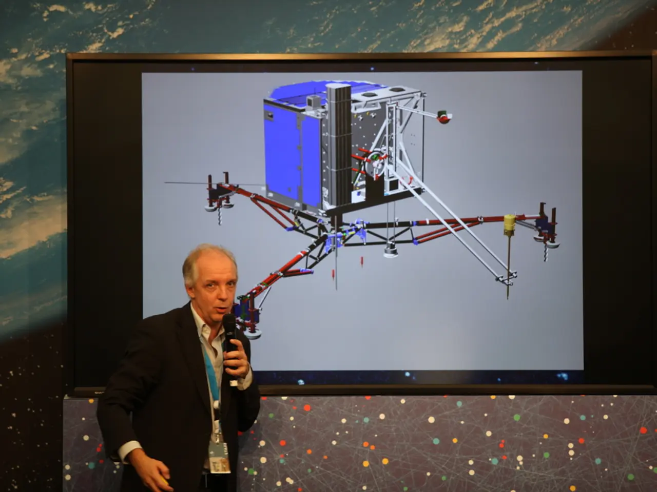 The man in front of the picture wearing a white shirt and black blazer is holding a microphone in...