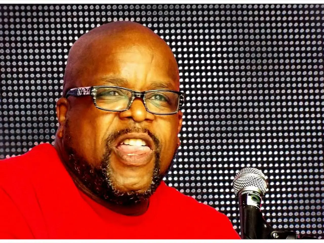 In this image, we can see a person wearing spectacles. We can also see a microphone. We can see the...