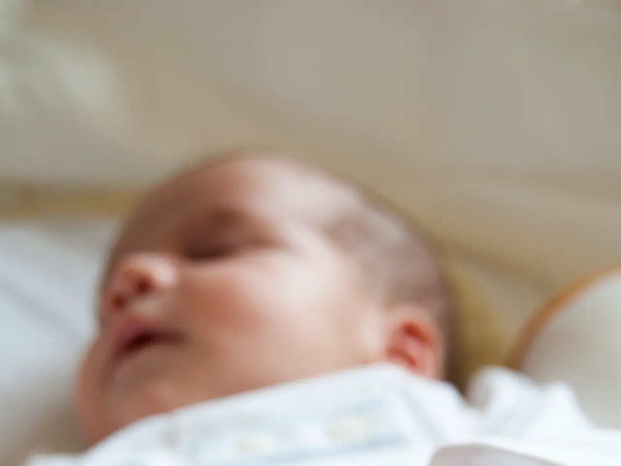 In this picture there is a baby. The baby is wearing a white dress. The background is blurred.