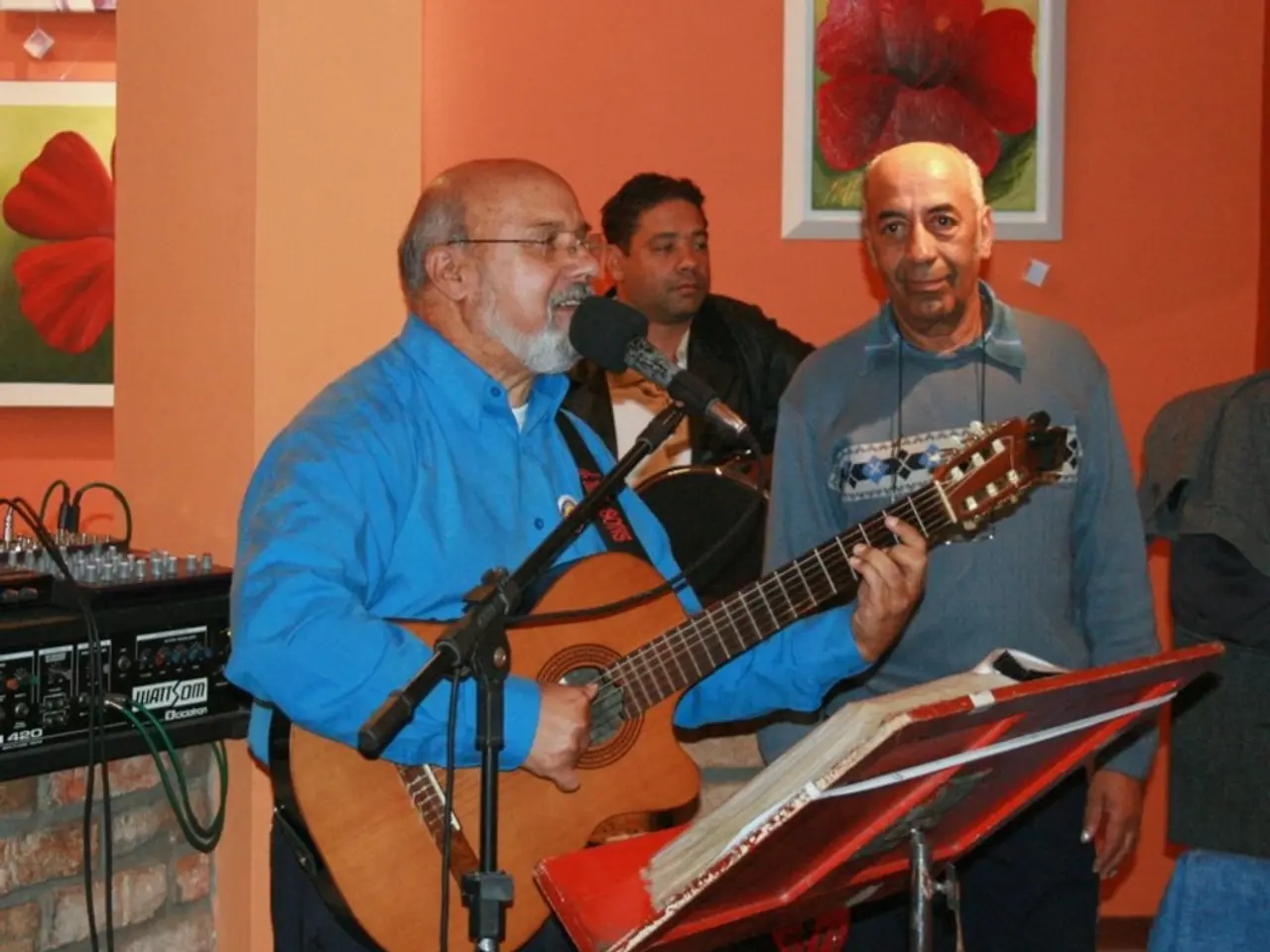 In this picture there are three men. The men with the blue shirt is playing guitar and singing...