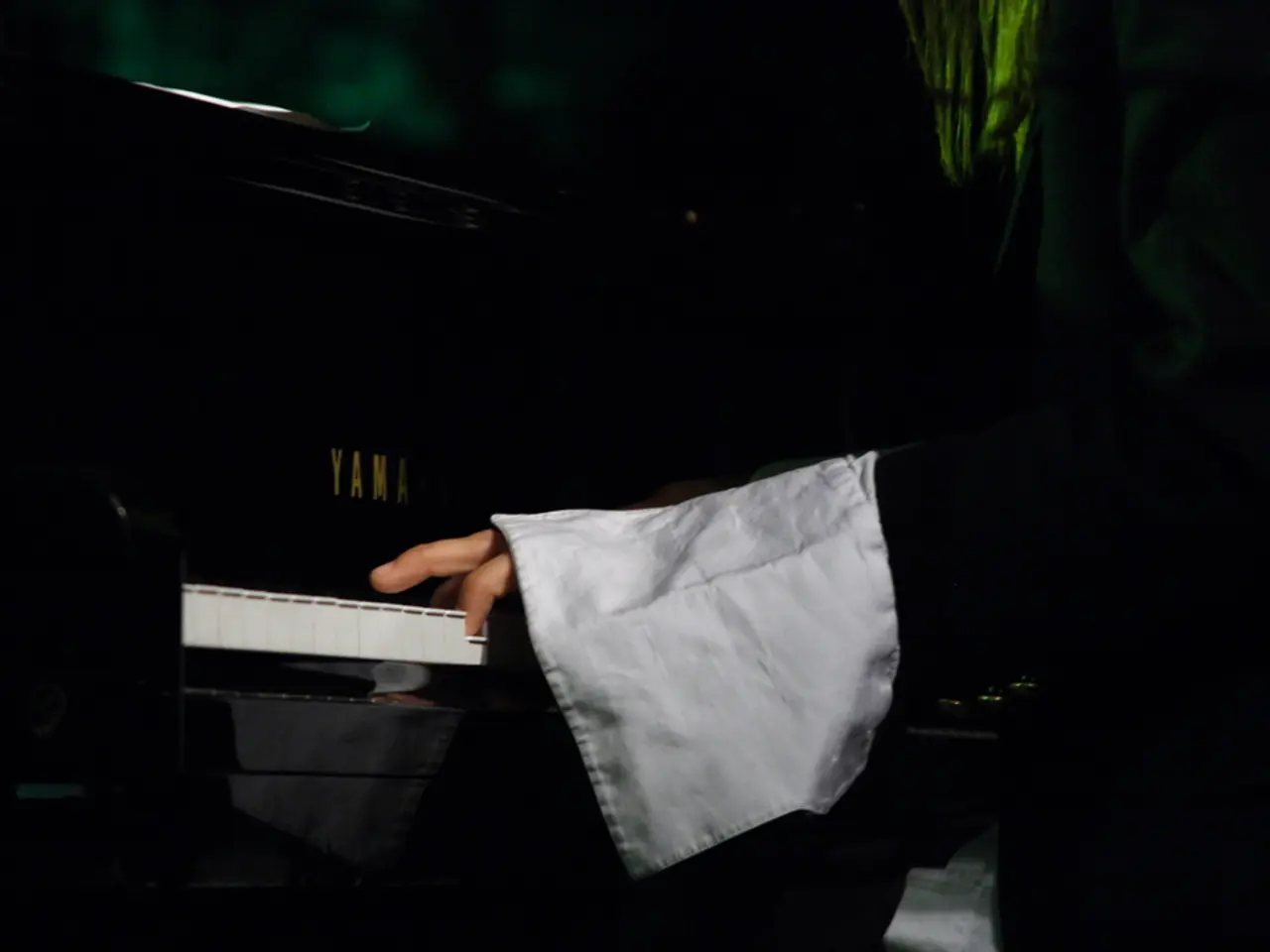 There is a person playing a piano. On the piano something is written. In the background it is...