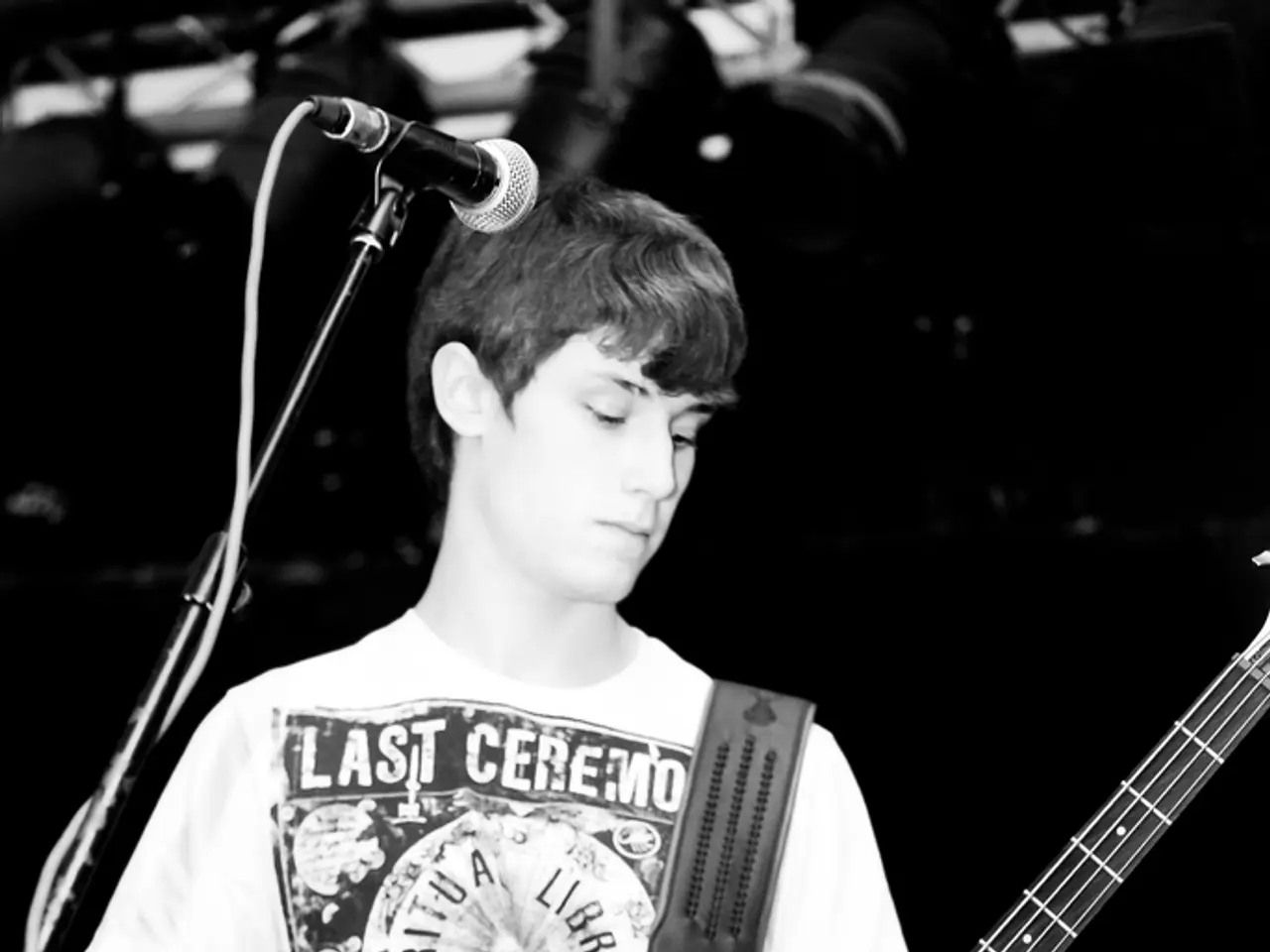 This picture describe a boy wearing white t- shirt and skull printed on it, holding a guitar and...