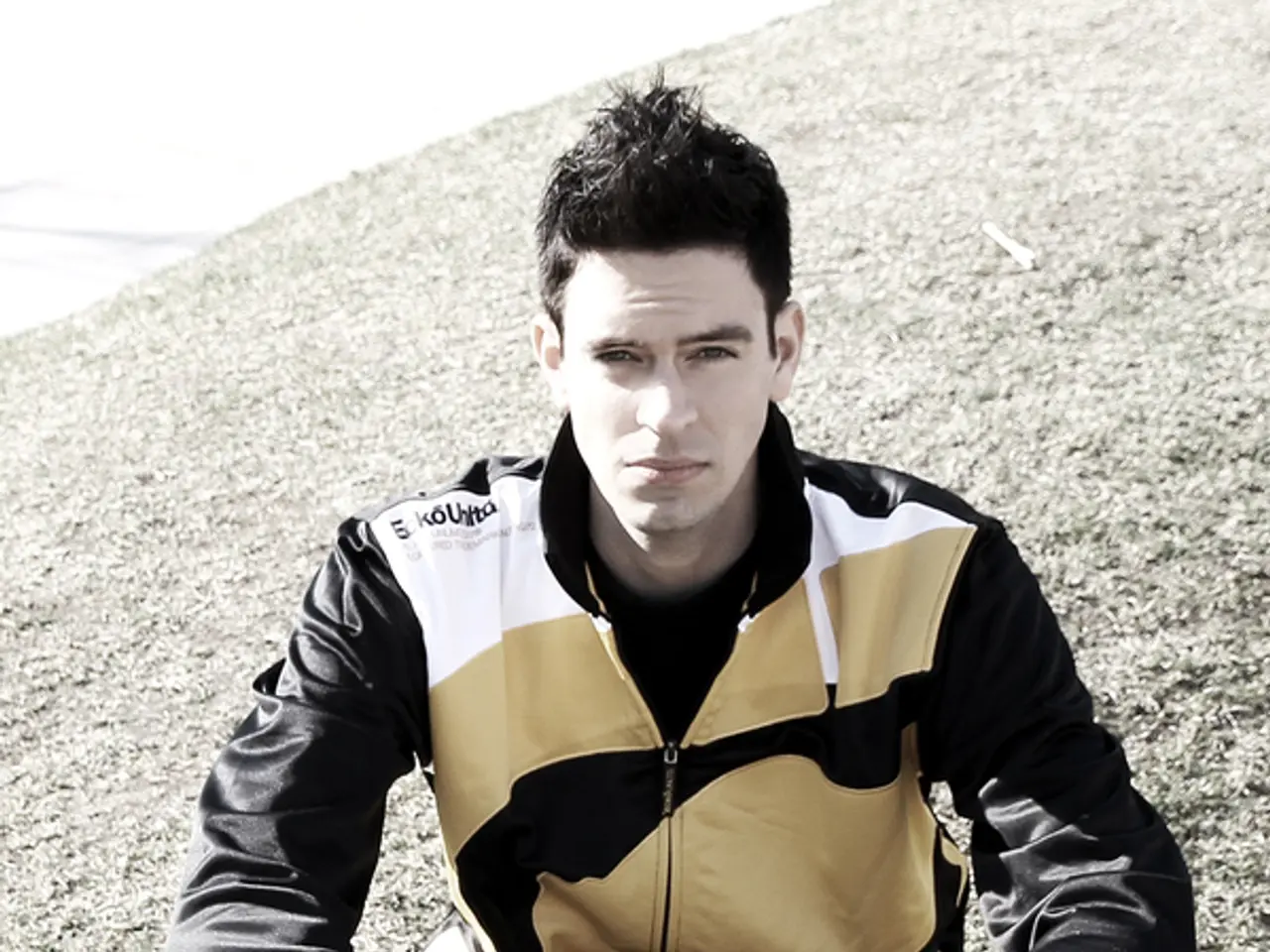 In this image we can see a man sitting on the grass. He is wearing a jacket and a pant. Here we can...