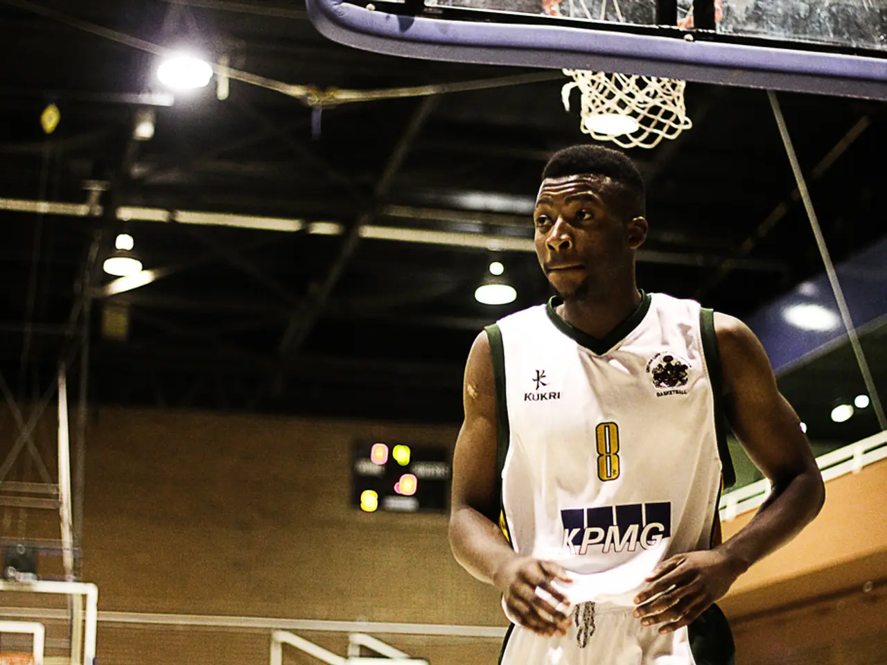 In the foreground of this picture, there is man in white sports dress in a basketball court. In the...