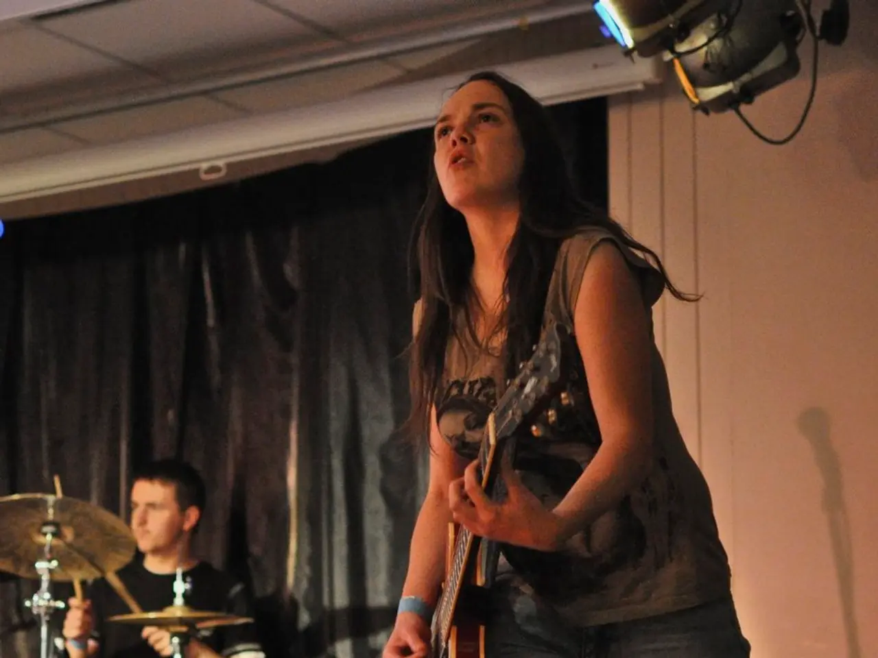 This image is clicked in a musical concert. There are two persons in this image. One is woman and...