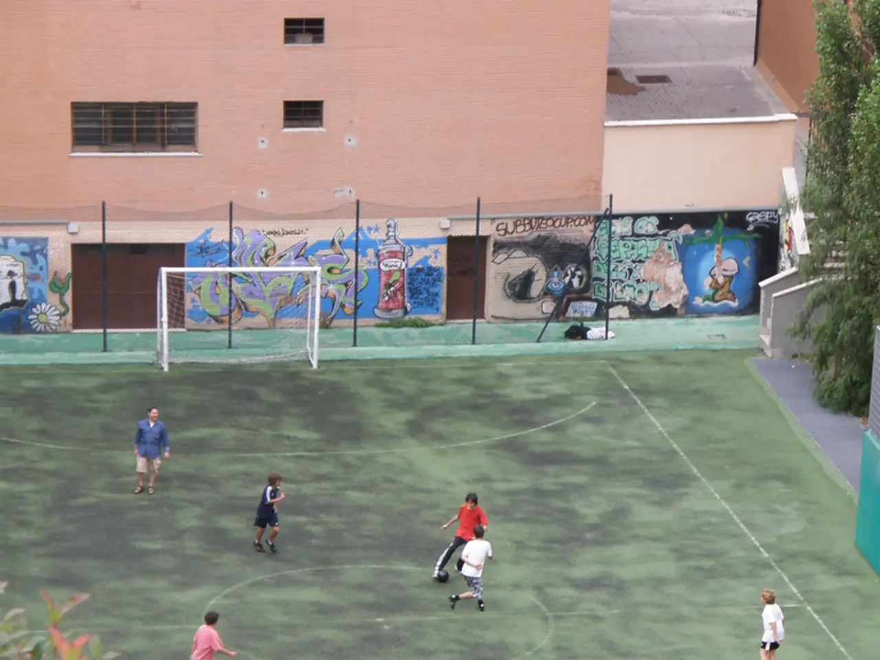 In this image we can see children playing football. There are goal posts. In the background of the...
