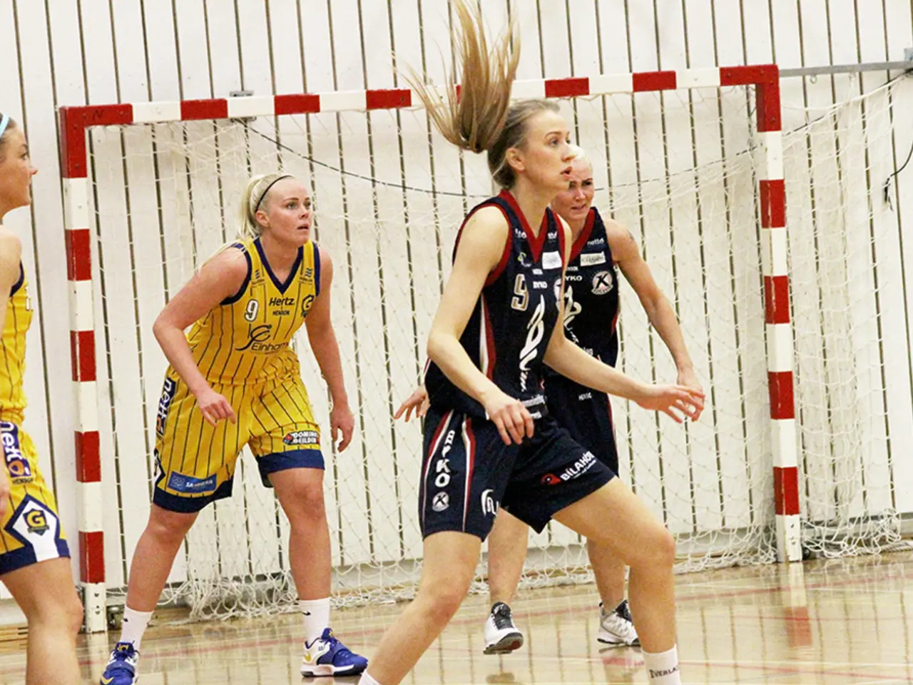 In this image there are women playing. In the background there is a net and there is a stand which...