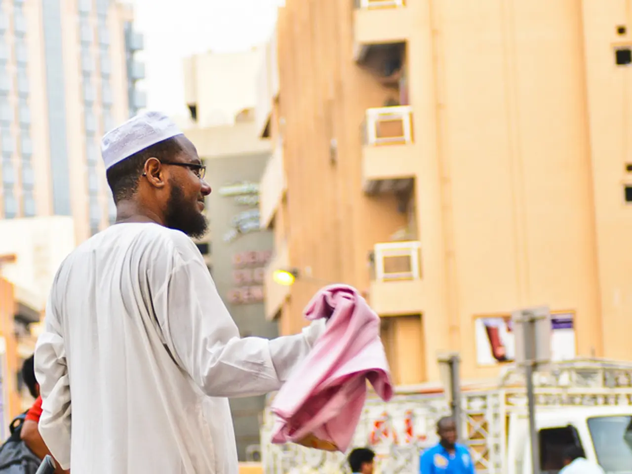 I can see in this image a man standing on the road with a child on wheels. In the background I can...
