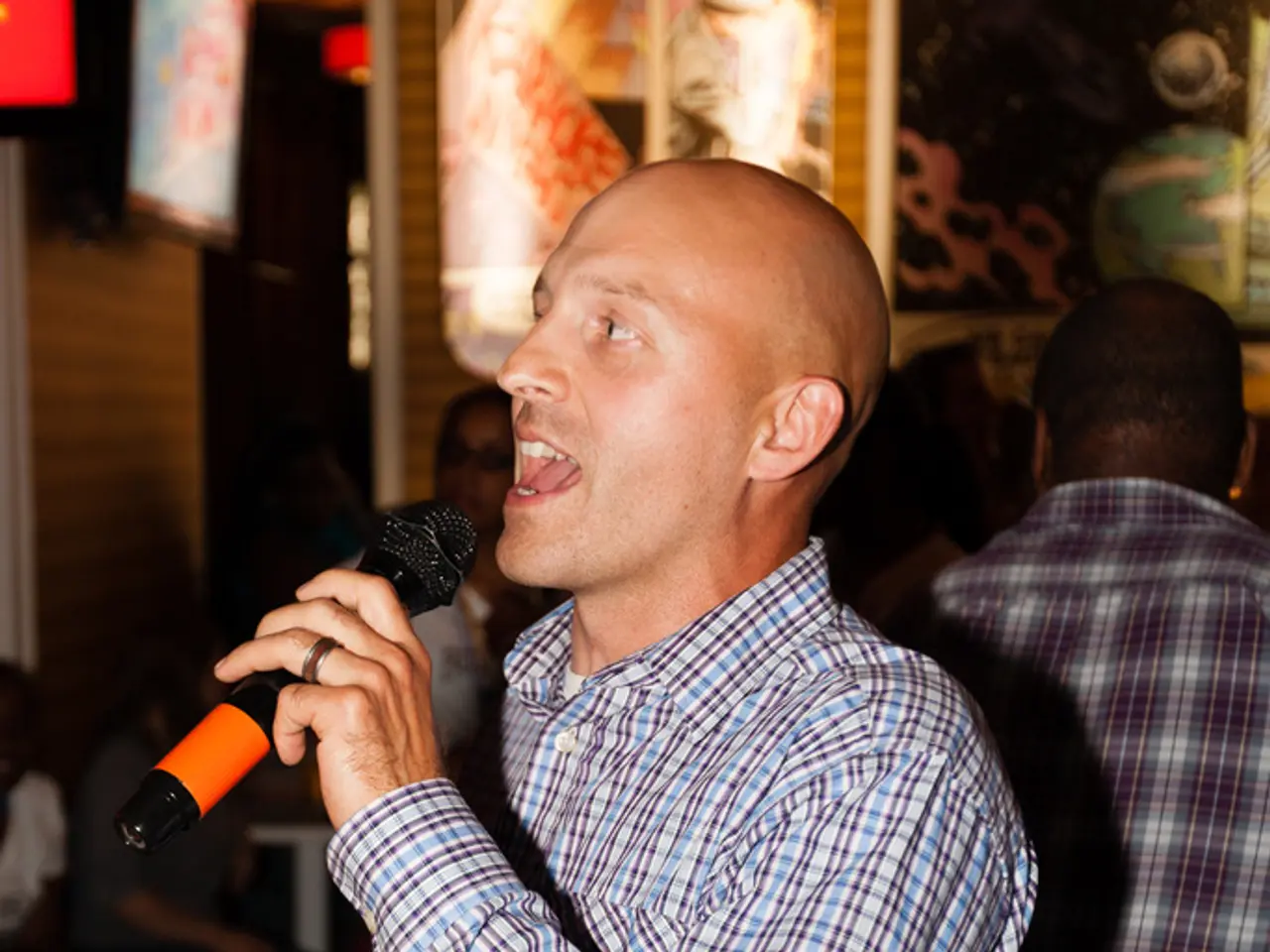 The person wearing a black belt is standing and singing in front of a mike and there are also a...