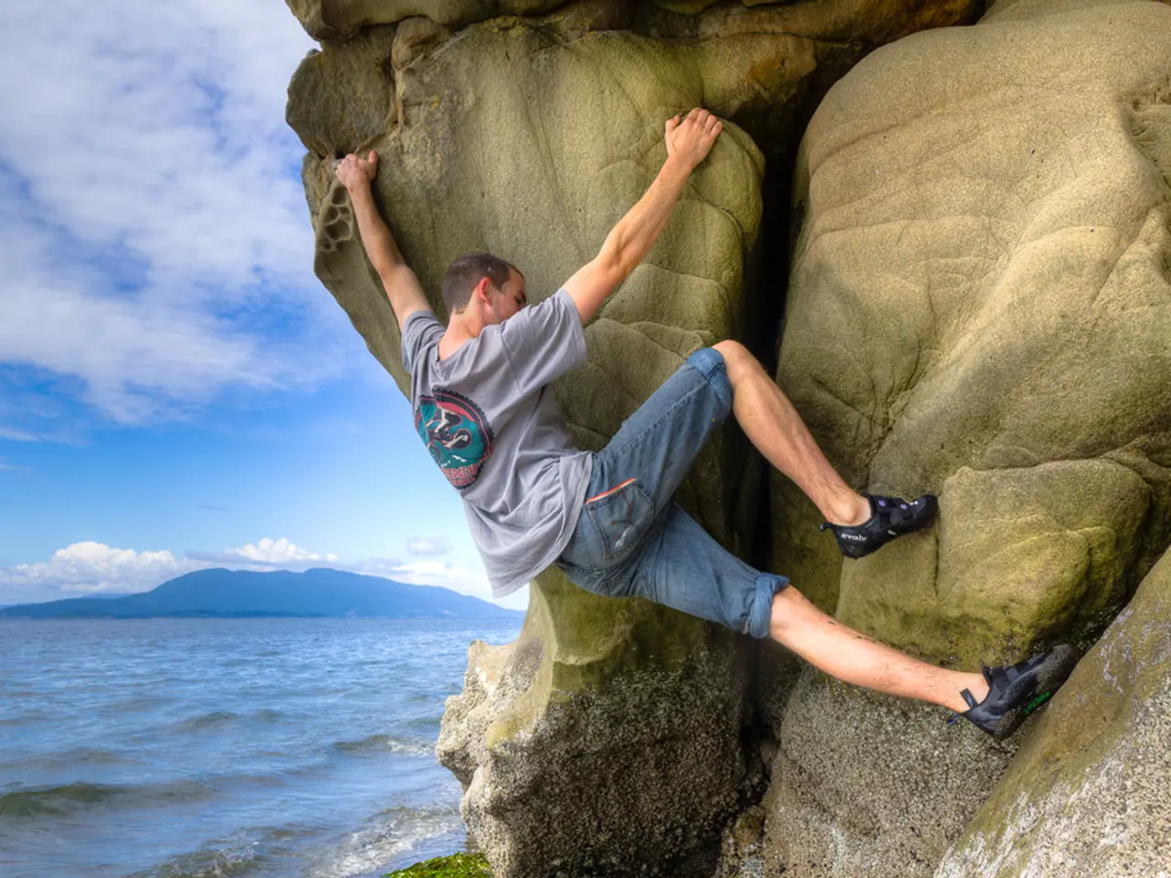 In this image we can see a person climbing a mountain. On the left side, we can see the water,...