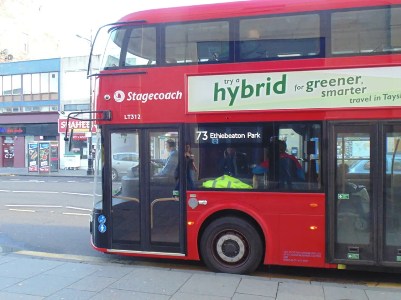 In the foreground of the picture there is payment and a bus. On the left there are buildings,...