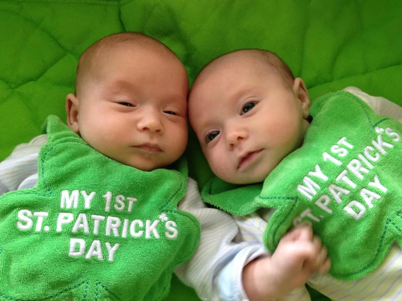 In the center of the image there are two babies. In the background of the image there is a green...