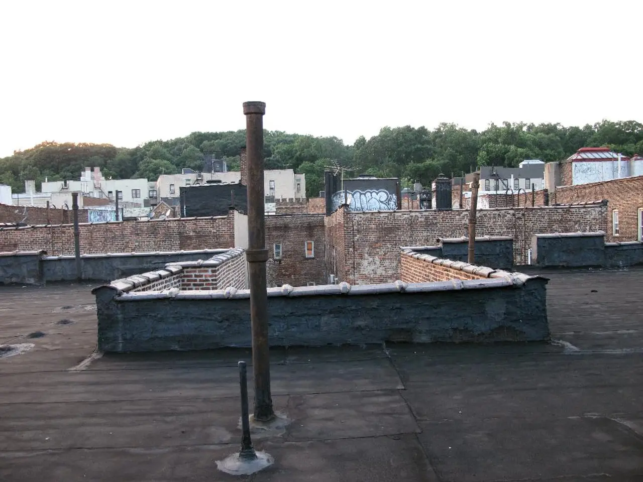 In this picture I can see buildings and few poles and I can see trees and a cloudy sky.