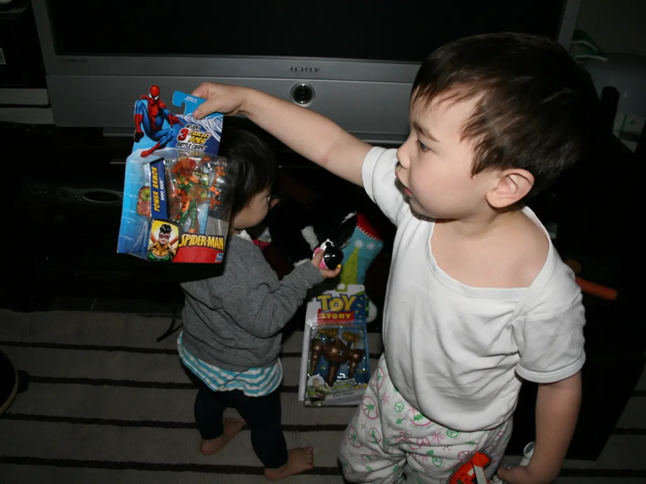 In this image we can see two kids who are wearing white and ash color dresses holding spider-man...