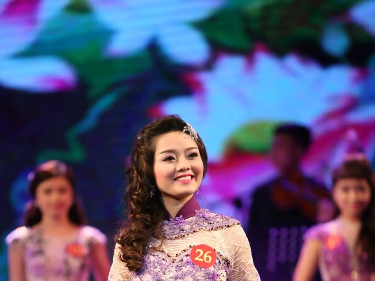 In this image we can see a woman with cream and purple color dress and a badge attached to her...