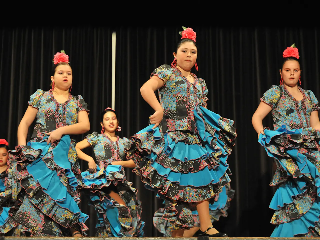 This picture shows few women dancing on the dais and we see black color cloth on the back. All the...