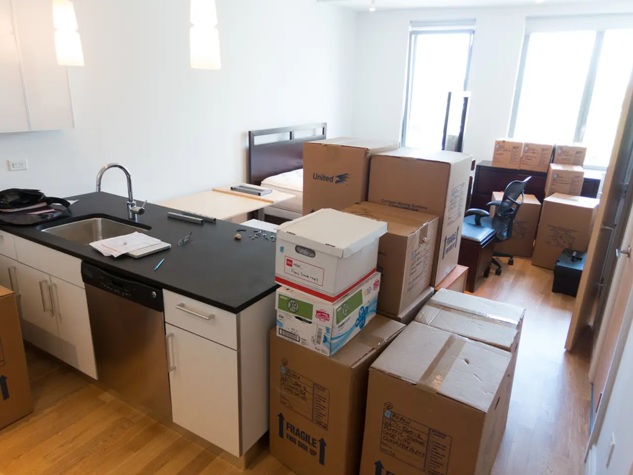 This picture is clicked inside a room. There are many cardboard boxes in the room. There is also a...