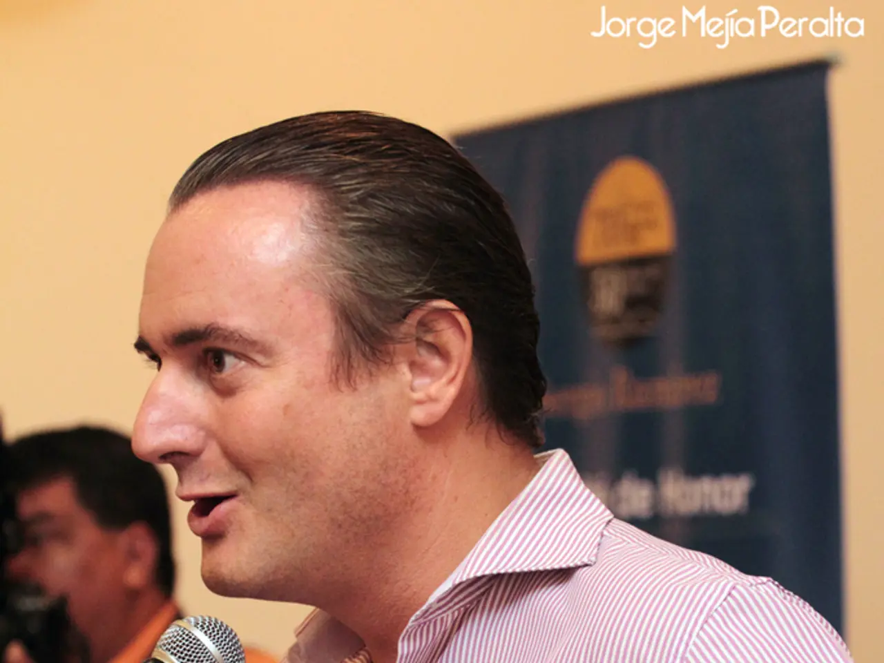 This is the man standing and talking in the mike. At background I can see a poster attached to the...