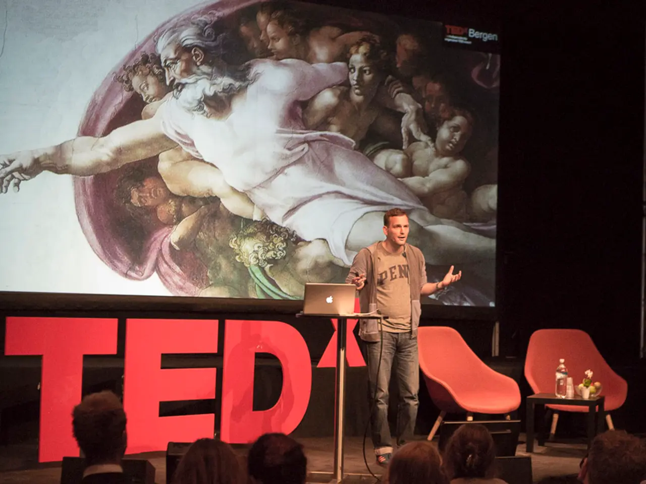 This is clicked on a stage. There is screen on the backside. There are chairs and there is a person...