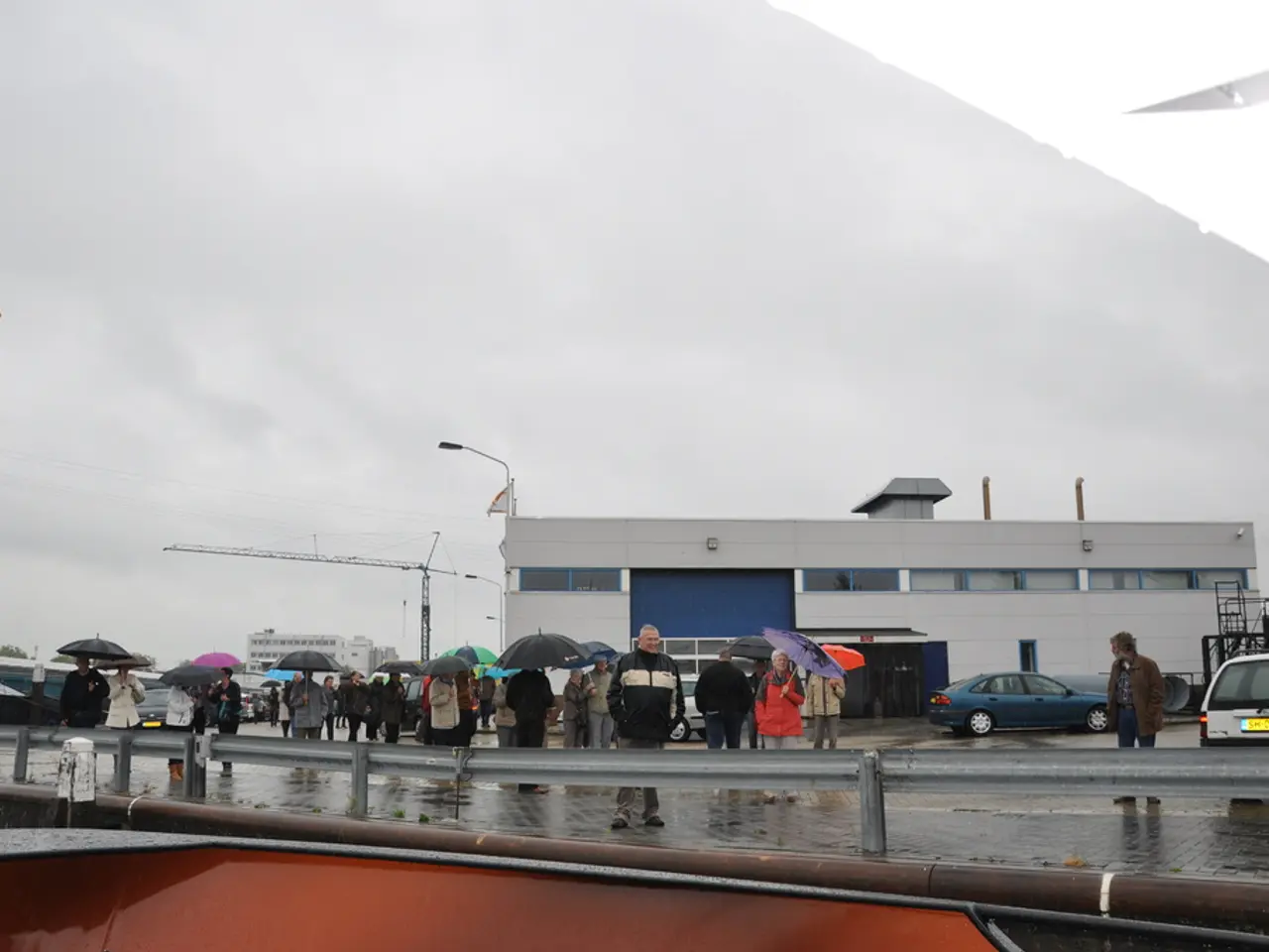 There are groups of people standing and few people are holding umbrellas. This is the flag hanging...