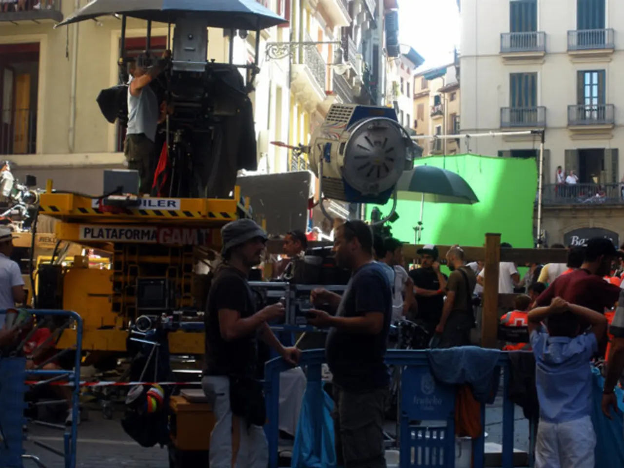In this image there are a few people standing, in between them there is a film shooting equipment...