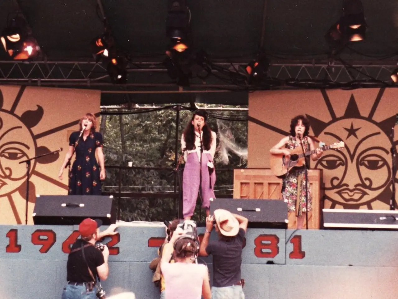 In this picture we can see three girls standing on the stage, two are singing on the microphone and...