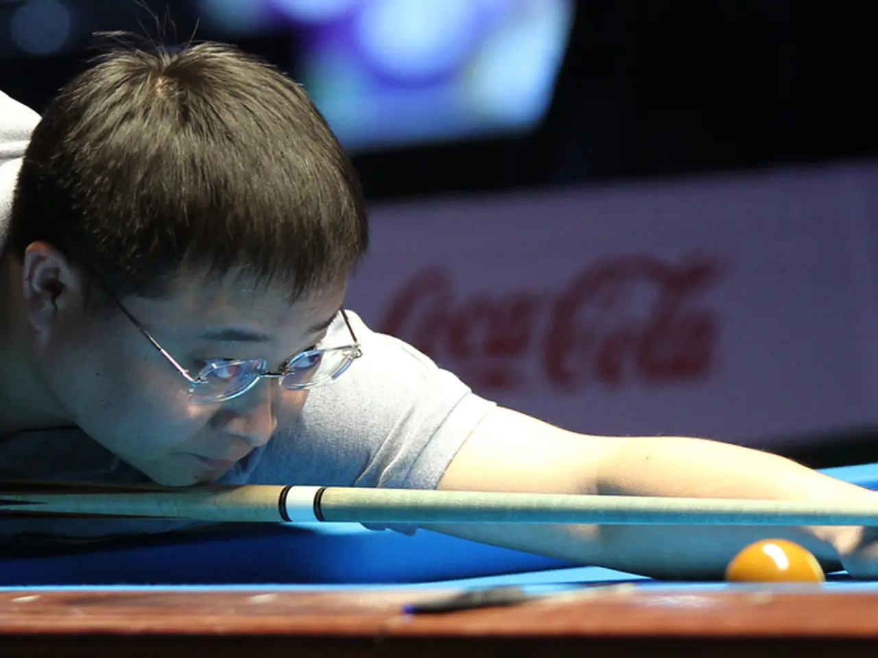 In the image, a man is playing snooker game and the background is blurry.