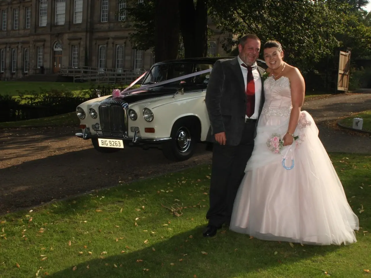 In this image, we can see a bride and a groom and one of them is holding flowers and an object. In...