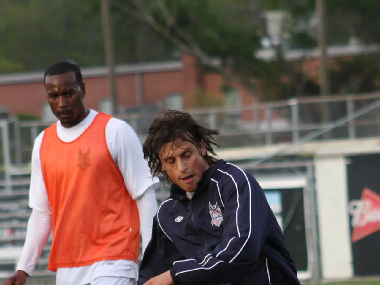 In this picture there are two football player. In the front there is a player wearing a black color...