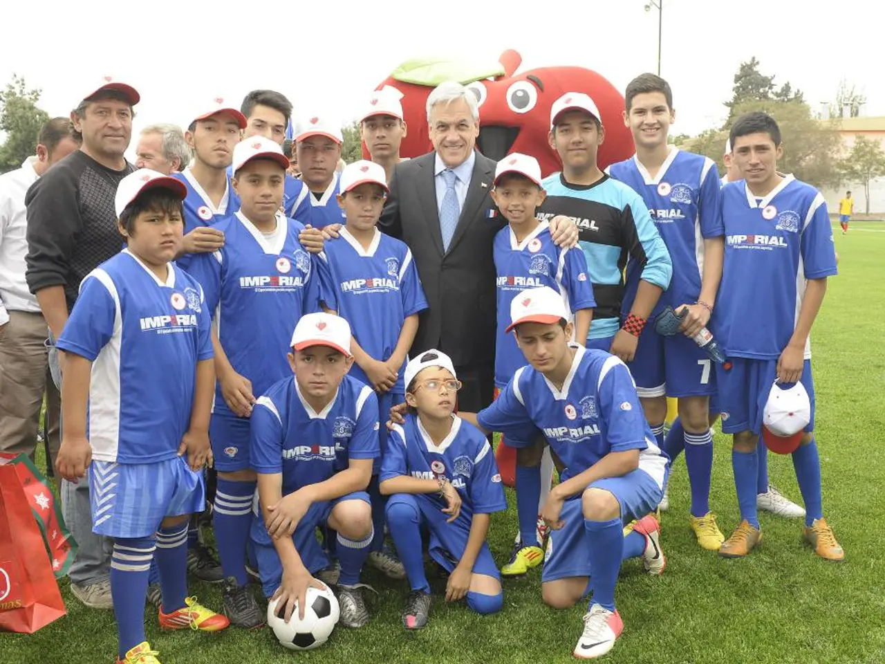 In the picture we can see some boys and few men are standing, and a man who is wearing a blazer,...