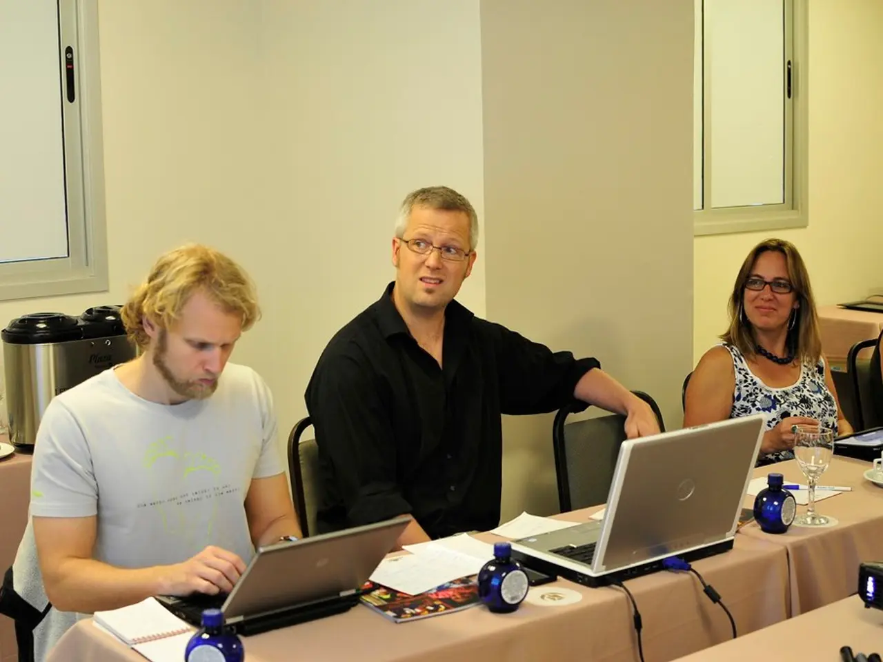 This is an inside view of a room. Here I can see two men and two women are sitting on the chairs in...