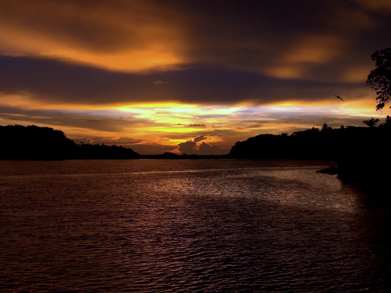 In this image, we can see few mountains, trees, cloudy sky. At the bottom, there is a sea.