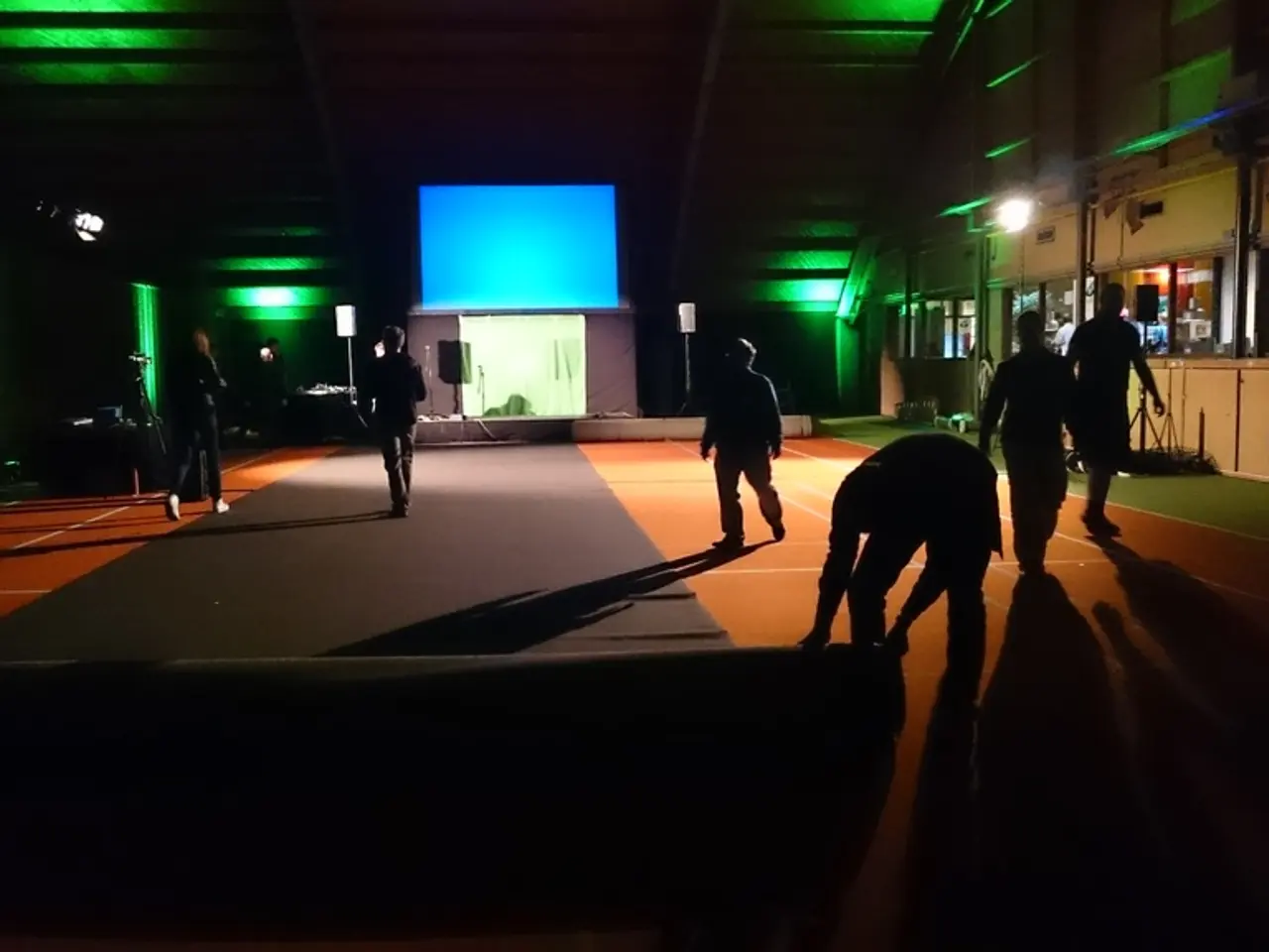 In this image, we can see a dark room, there is carpet on the floor, there are some people walking...