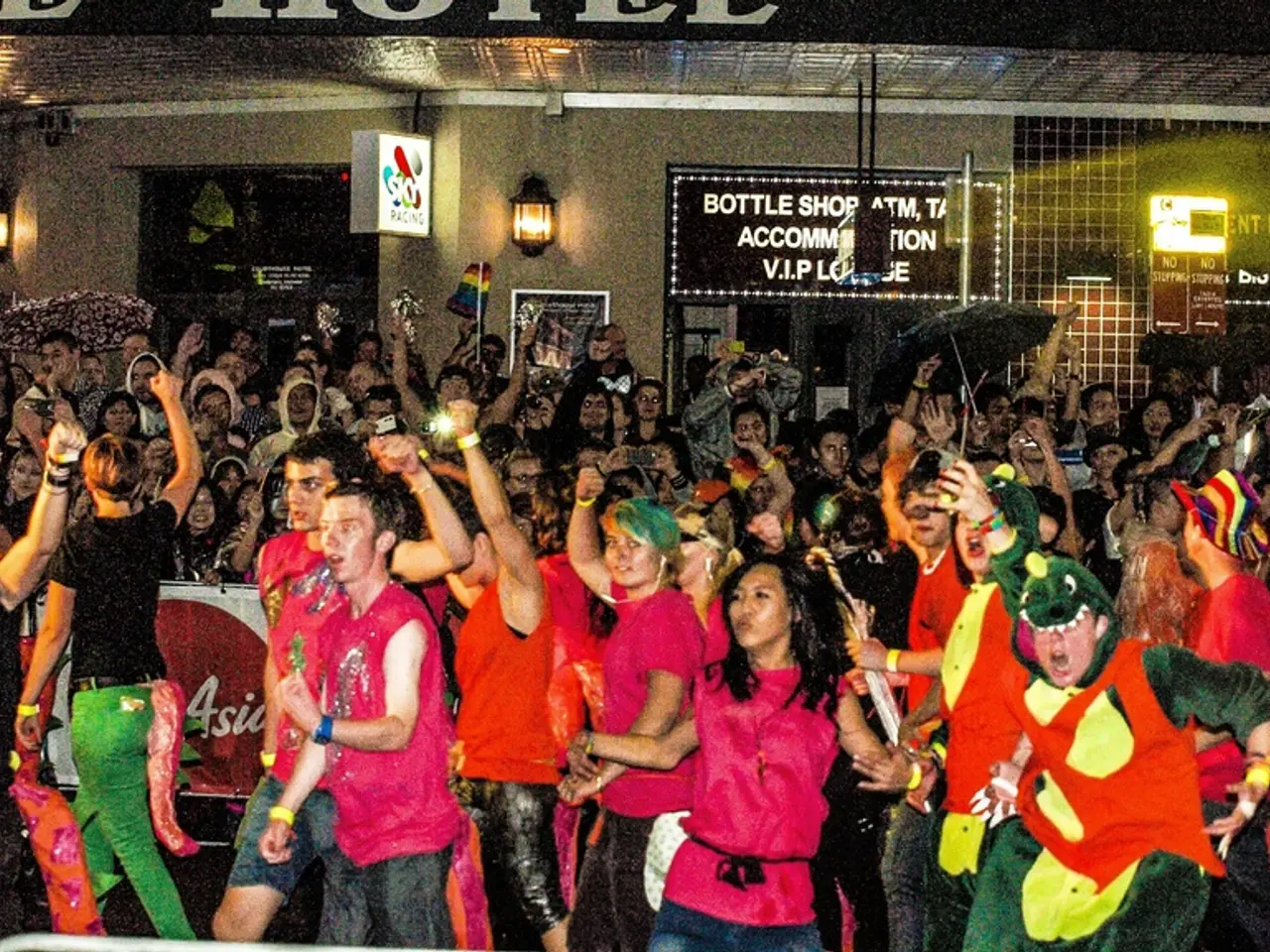 In this image there are many people. They are dancing and enjoying. Behind them there is a banner...