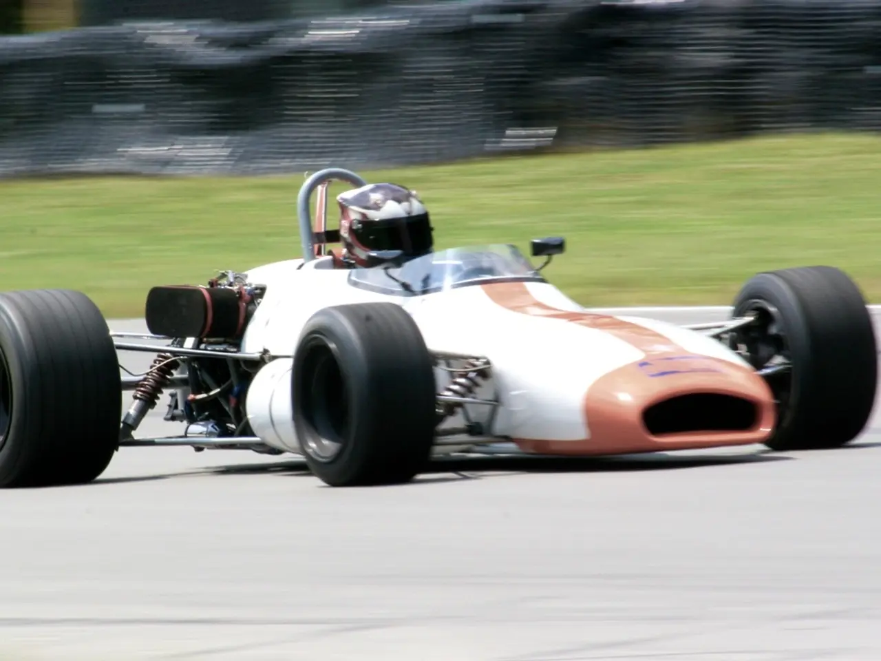 In this image, we can see a racing car, there is a person sitting in the car and wearing a helmet....