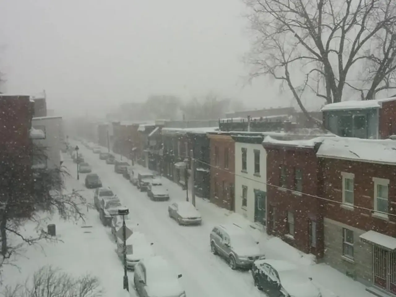 There is a road which has cars and buildings on either sides of it covered with snow and there are...