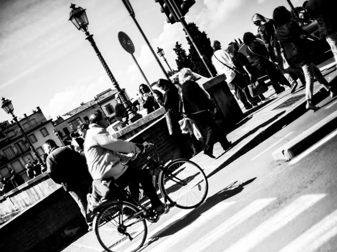 It is a black and white picture where people are walking on the road and one person is riding a...