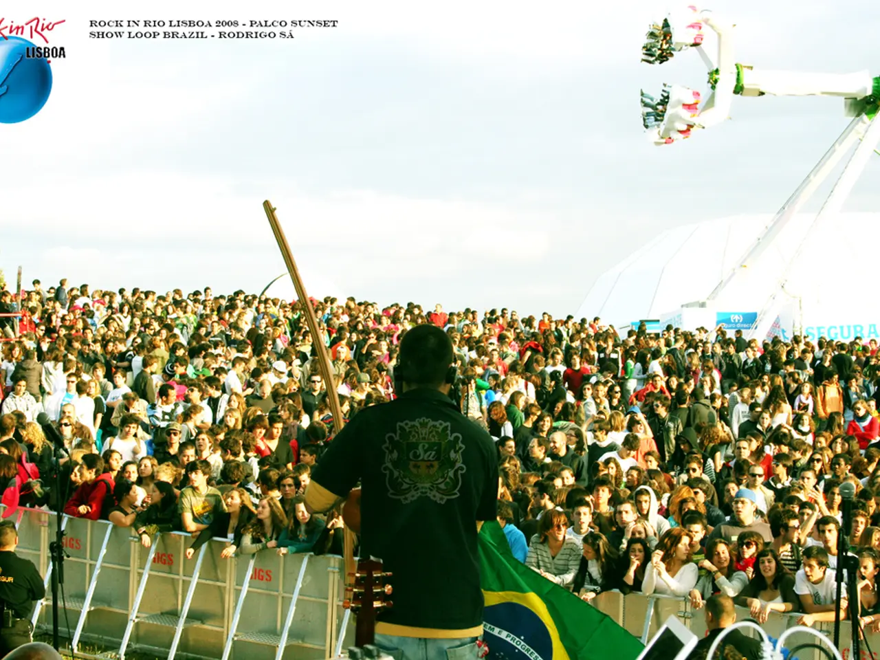 In this picture we can see a man wearing black color t-shirt standing on the stage playing guitar....